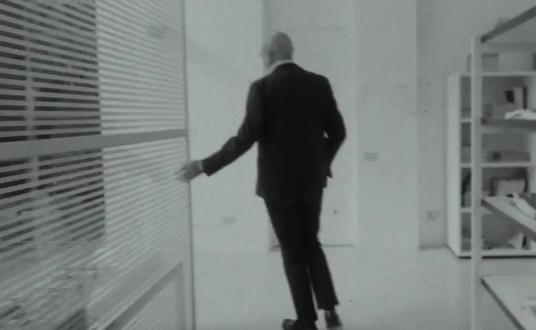 Arquiteto Piero Lissoni de costas com a mão em uma parede de vidro